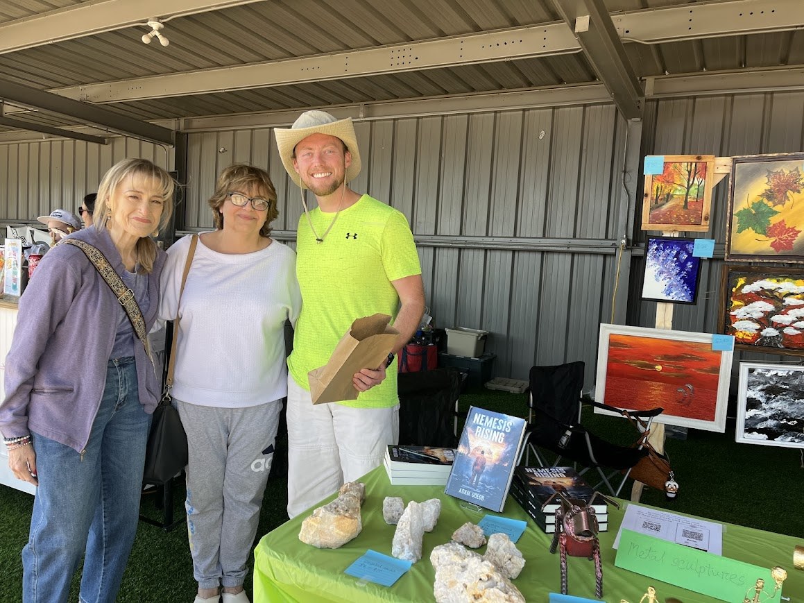 Adam with visitors beside a display of books, paintings, and sculptures