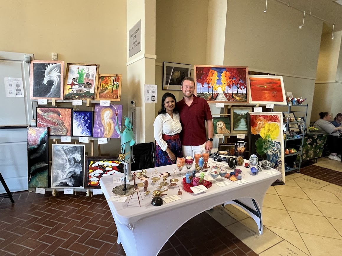 Adam and Fahmida with their paintings, sculptures, and books at a market