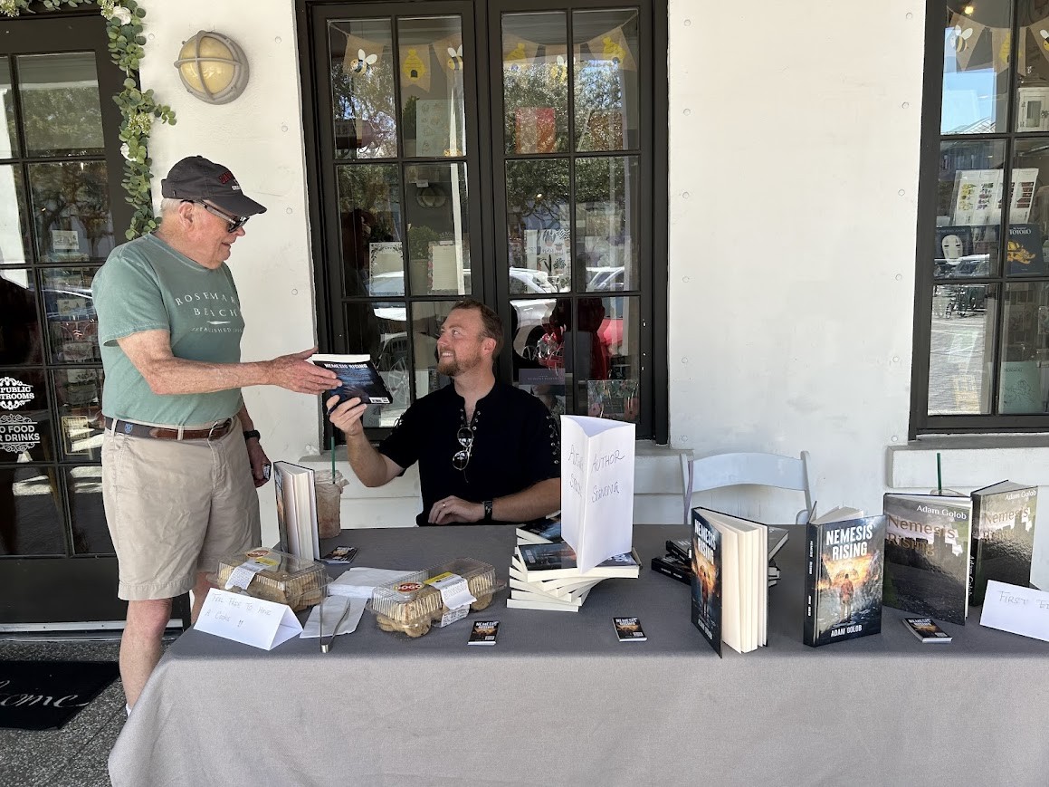 Adam sharing a copy of Nemesis Rising with a reader at a signing event