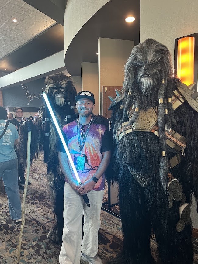 Adam with a glowing lightsaber beside two costumed Wookiees
